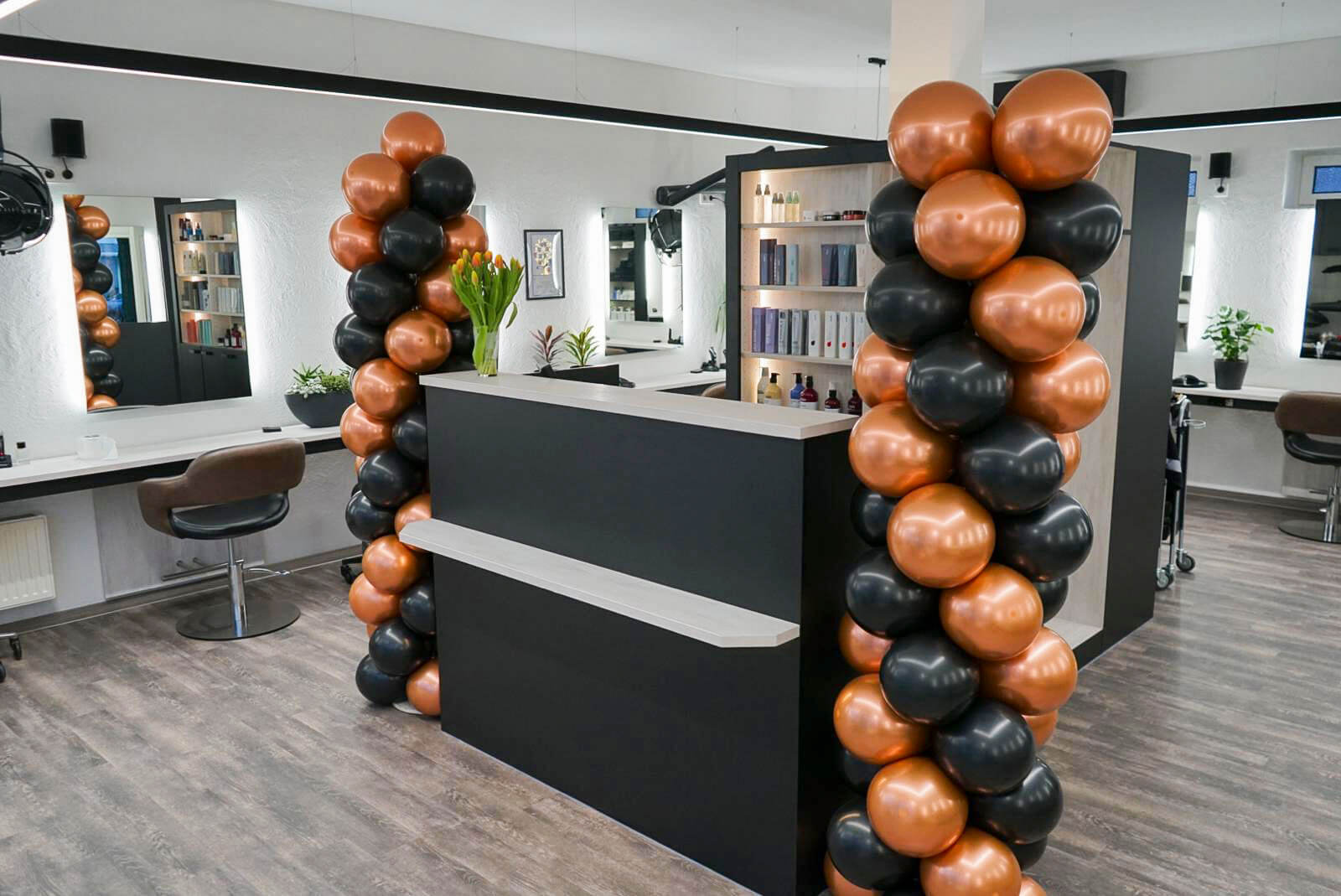 Friseursalon mit stilvoller Einrichtung, schwarzer Empfangstheke und Ballondekoration